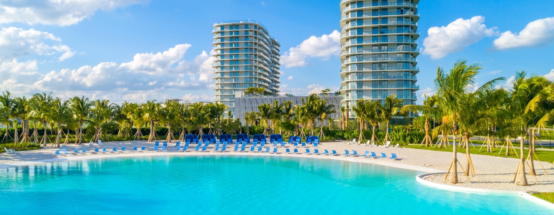 a body of water with sand palm trees and buildings behind it